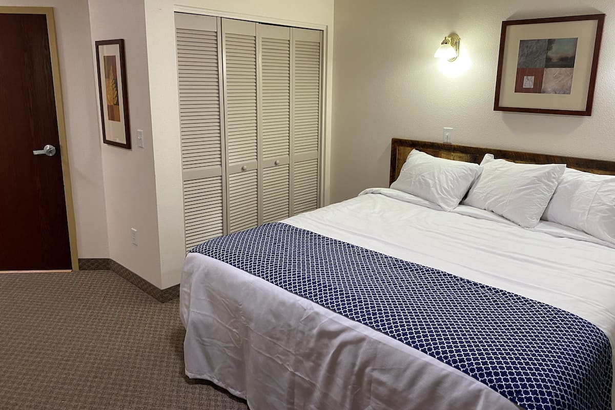 A hotel room with a bed, a closet, a door, and a wall-mounted light fixture.