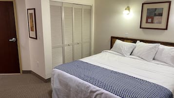 A hotel room with a bed, a closet, a door, and a wall-mounted light fixture.