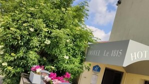 Un hotel llamado 'HOTEL Le 1815' con un cartel, un camino pavimentado y macetas con flores a lo largo del lateral.