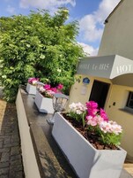 Un hotel llamado 'HOTEL Le 1815' con un cartel, un camino pavimentado y macetas con flores a lo largo del lateral.