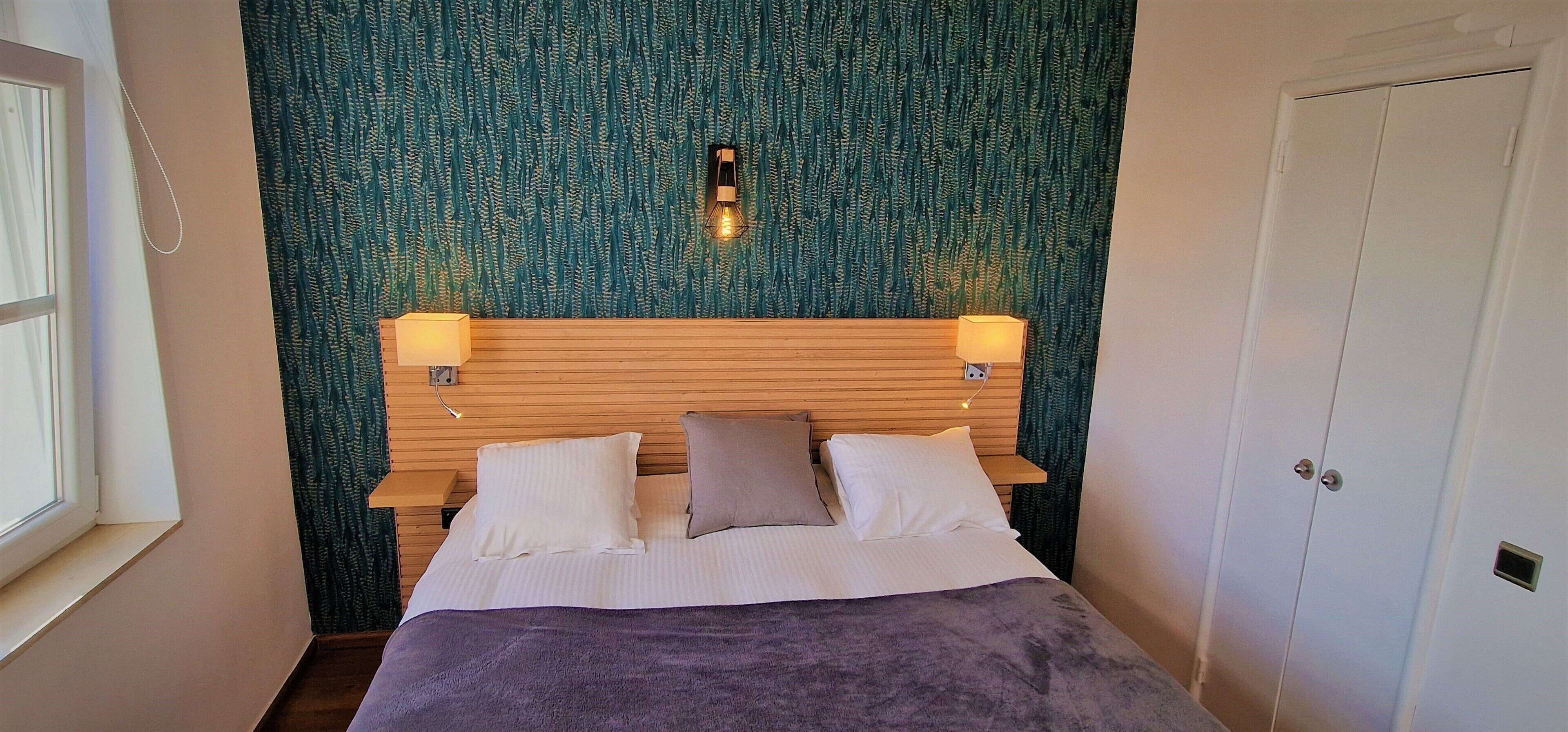 Een slaapkamer met een houten hoofdbord, twee bedlampen, een bed met witte lakens en een groene, geribbelde wand.