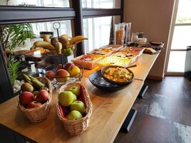 Una mesa de buffet con diversas frutas y platos, incluyendo manzanas, plátanos y un tazón de frutas mixtas.
