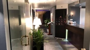 Un pasillo moderno de hotel con un separador de vidrio, un mostrador de recepción, una planta en maceta y una lámpara.