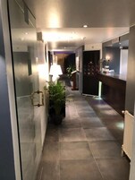 Un pasillo moderno de hotel con un separador de vidrio, un mostrador de recepción, una planta en maceta y una lámpara.