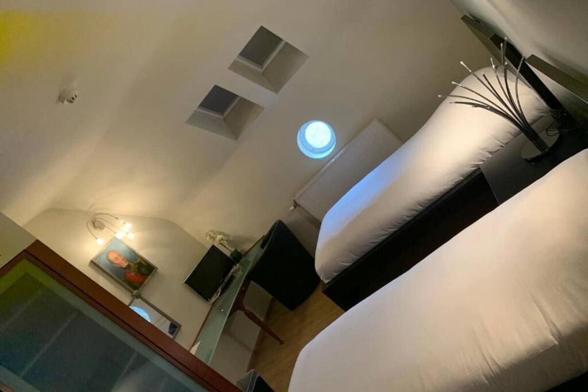 A hotel room with a bed, a desk, a chair, a small table, and a wall-mounted TV.