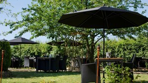 Un patio al aire libre con mesas y sillas bajo sombrillas, rodeado de follaje.