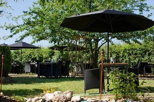 Un patio al aire libre con mesas y sillas bajo sombrillas, rodeado de follaje.