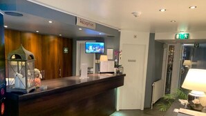 Un área de recepción con un mostrador de madera oscura, un televisor montado en la pared y un letrero de recepción.