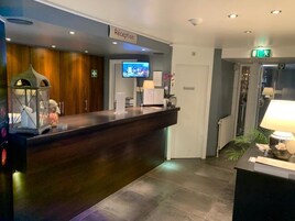 Un área de recepción con un mostrador de madera oscura, un televisor montado en la pared y un letrero de recepción.