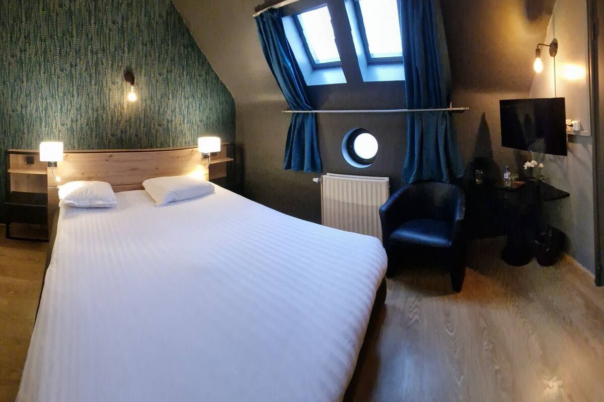 A hotel room with a bed, a desk, a chair, a TV, a wardrobe, and a window with curtains.
