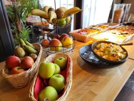Una mesa de buffet con diversas frutas y platos, incluyendo manzanas, plátanos y una ensalada de frutas.