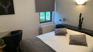 A bedroom with a bed, a window with a view, a radiator, a desk, and a chair.