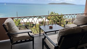 A balcony with two chairs and a table, overlooking a clear blue sea and a distant island. - Idyllic, Romantic Caribbean Ocean Front View Coakley Bay Condo. Quiet East End (Christiansted)