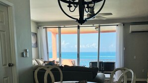 A dining area with a round table, white chairs, a chandelier, and a view of the ocean. - Idyllic, Romantic Caribbean Ocean Front View Coakley Bay Condo. Quiet East End (Christiansted)