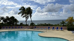A pool with blue chairs and palm trees, with a view of the ocean. - Idyllic, Romantic Caribbean Ocean Front View Coakley Bay Condo. Quiet East End (Christiansted)