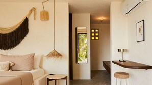 Una habitación moderna con cama, una pequeña mesa redonda, una lámpara colgante, una zona de bar con taburetes y vistas a la vegetación a través de una ventana.