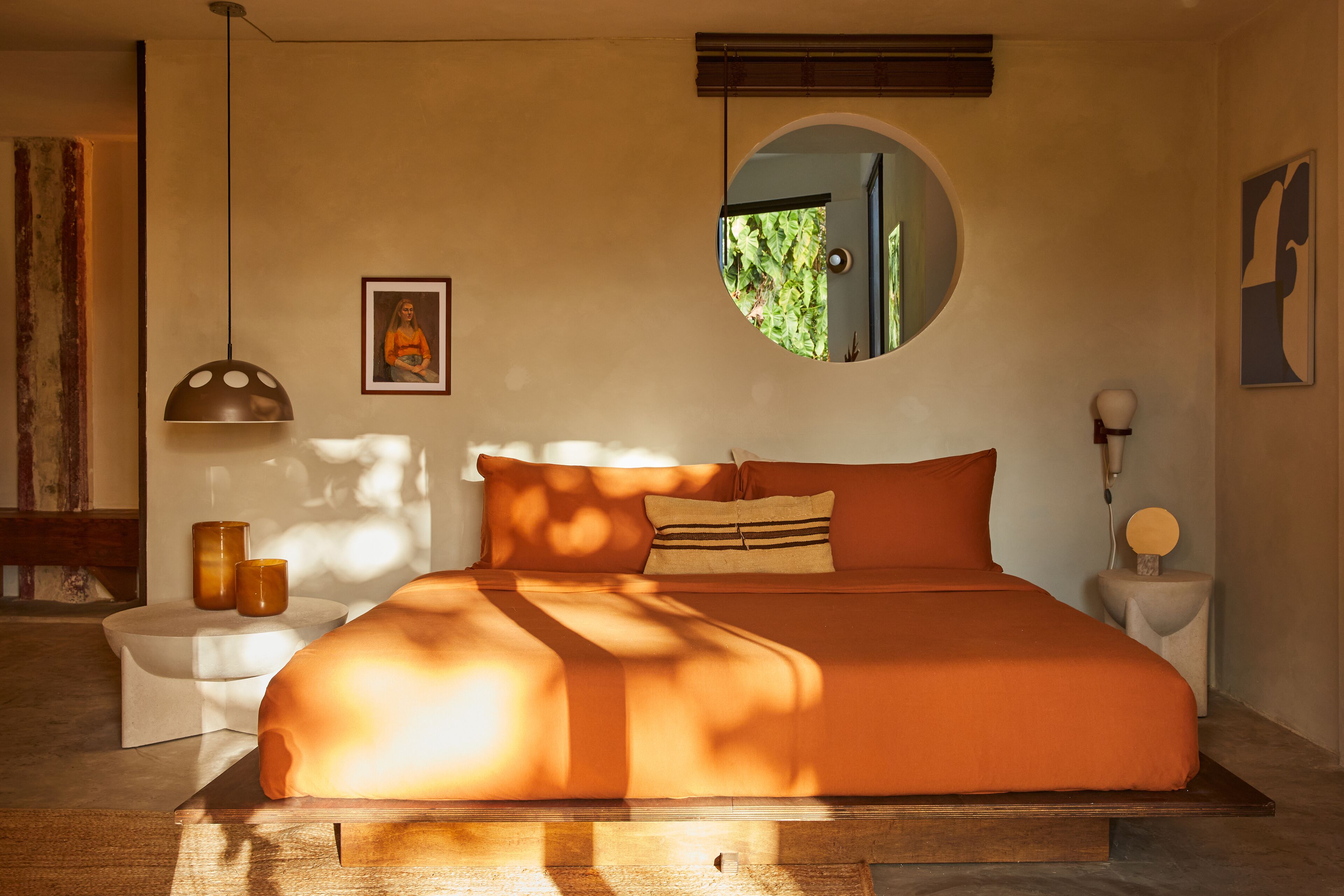 A bedroom with a large bed, a round mirror, and a small side table.