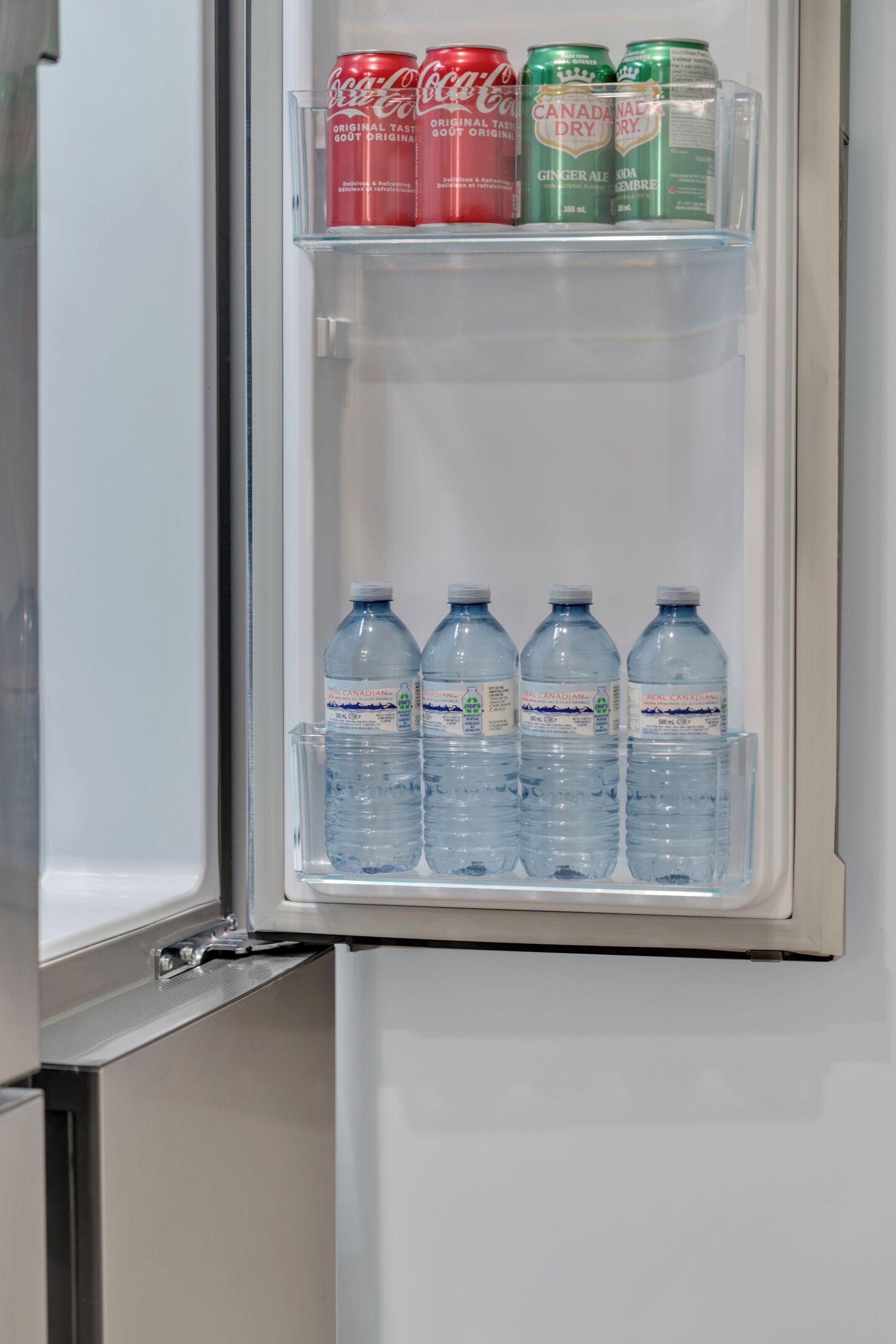 Ein Kühlschrank mit einer Ablage, auf der sich vier Wasserflaschen und drei Getränkedosen befinden.
