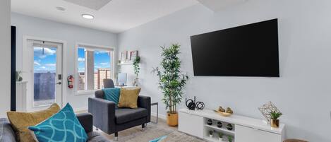 Un saló modern amb un sofà gris, una butaca negra, una taula consola blanca i un televisor negre gran fixat a la paret.