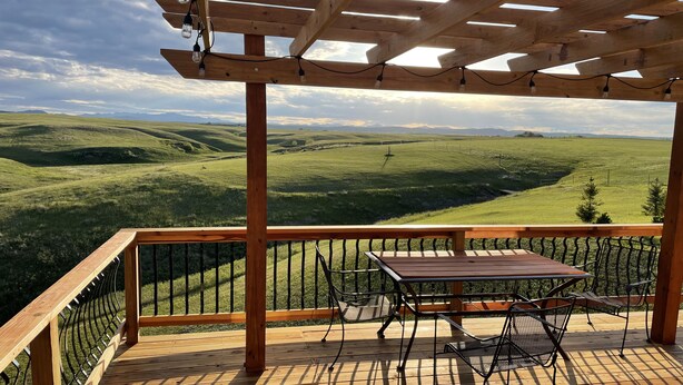 Eine Holzterrasse mit Tisch und Stühlen mit Blick auf ein grünes Tal.