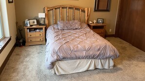 Ein Schlafzimmer mit Bett, Holz-Kopfteil, Nachttischen, einer Kommode und einer Tür.