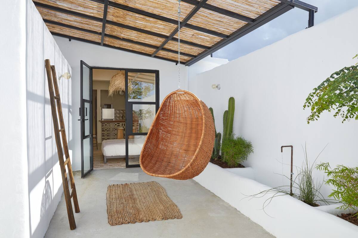 Un intérieur moderne agrémenté d’un fauteuil suspendu, d’une échelle et d’un cactus.