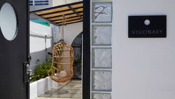 Una puerta con un letrero que dice "VISIONARY", un sillón colgante de mimbre y una pared blanca con paneles de vidrio.