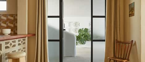 Quarto com porta de vidro deslizante que dá para área externa, uma cadeira de madeira, um banquinho e piso de azulejo.