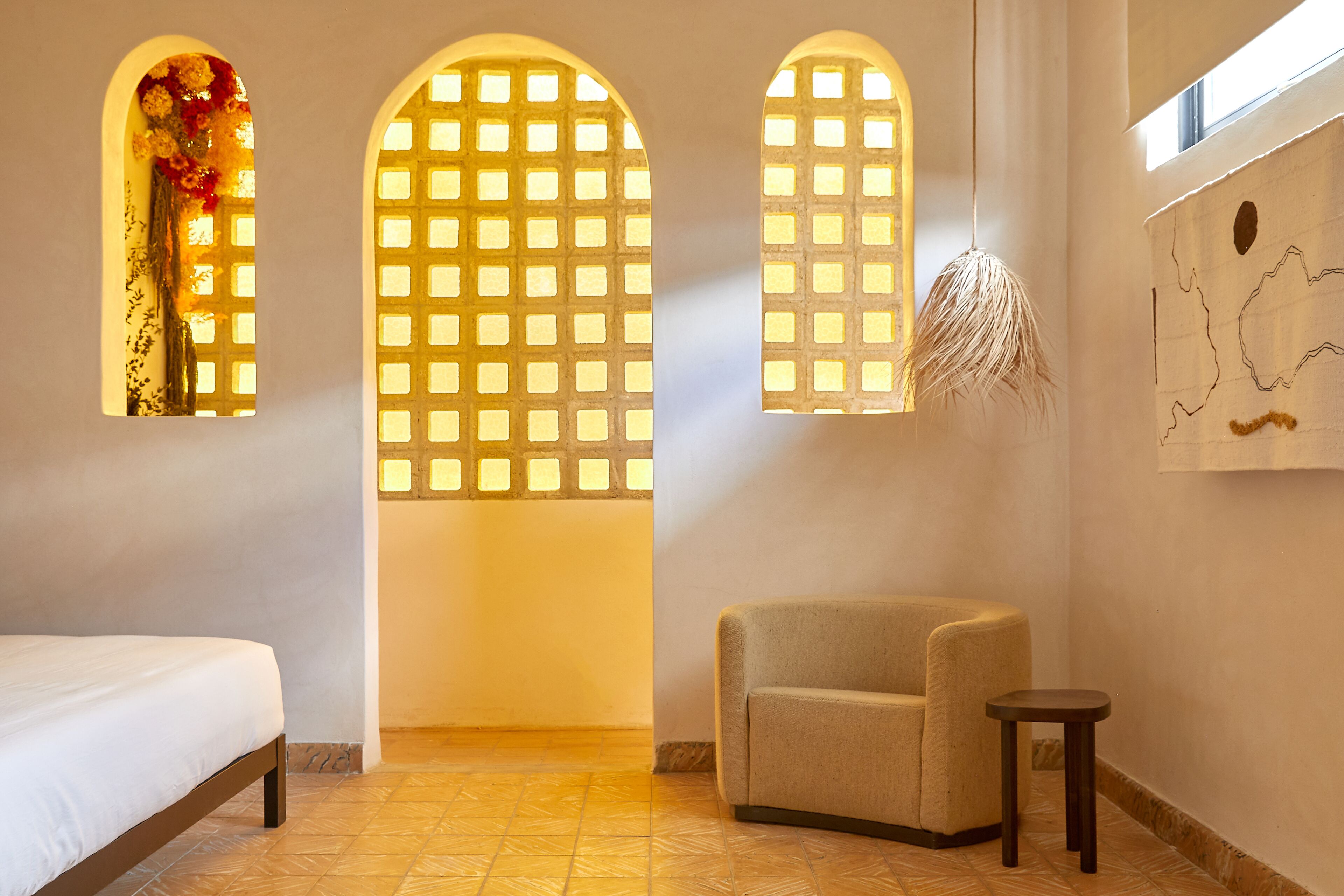A room with a bed, a chair, and three windows with decorative elements.