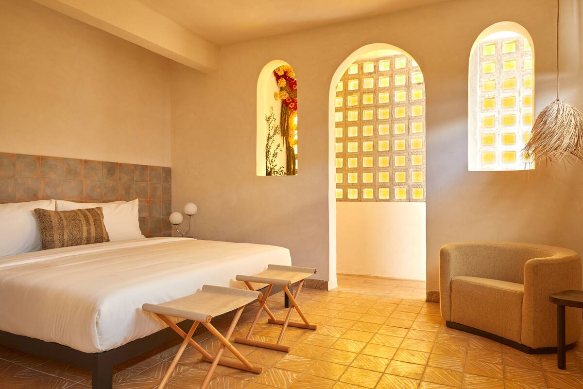 Une chambre d’hôtel avec un grand lit, un petit canapé et deux fenêtres agrémentées d’éléments décoratifs.