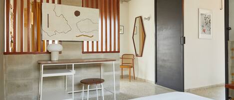 A bedroom with a bed, a desk with a chair, a map on the wall, and a door.