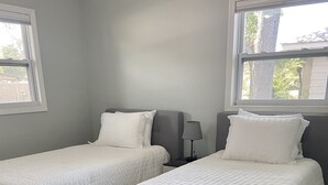 Una habitación con dos camas individuales, una mesita de noche con lámpara y una ventana con vistas a árboles.
