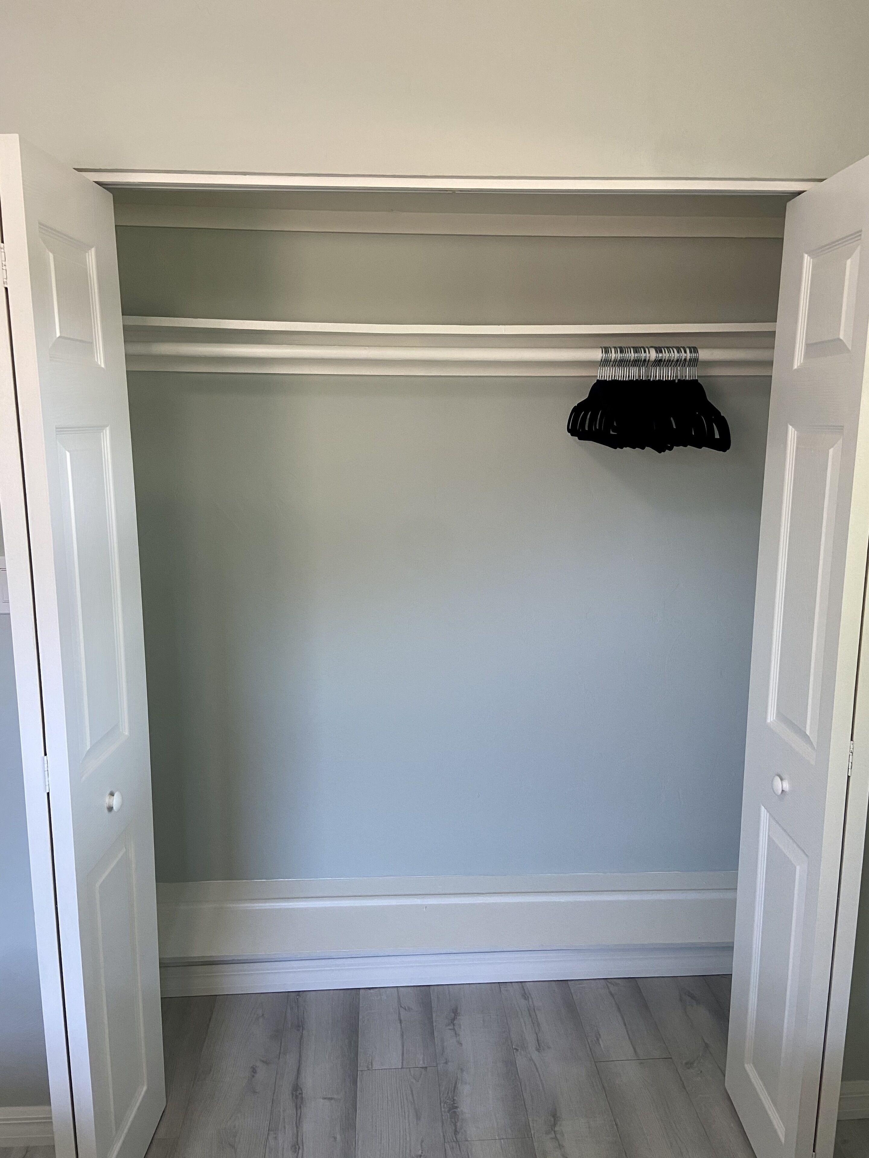A closet with white doors, a hanging rack, and a light grey wall.