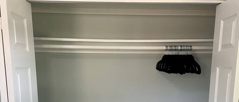A closet with white doors, a hanging rack, and a light grey wall.