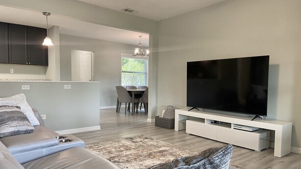 Una sala de estar moderna con un televisor de pantalla plana grande, un sofá y un comedor con sillas.