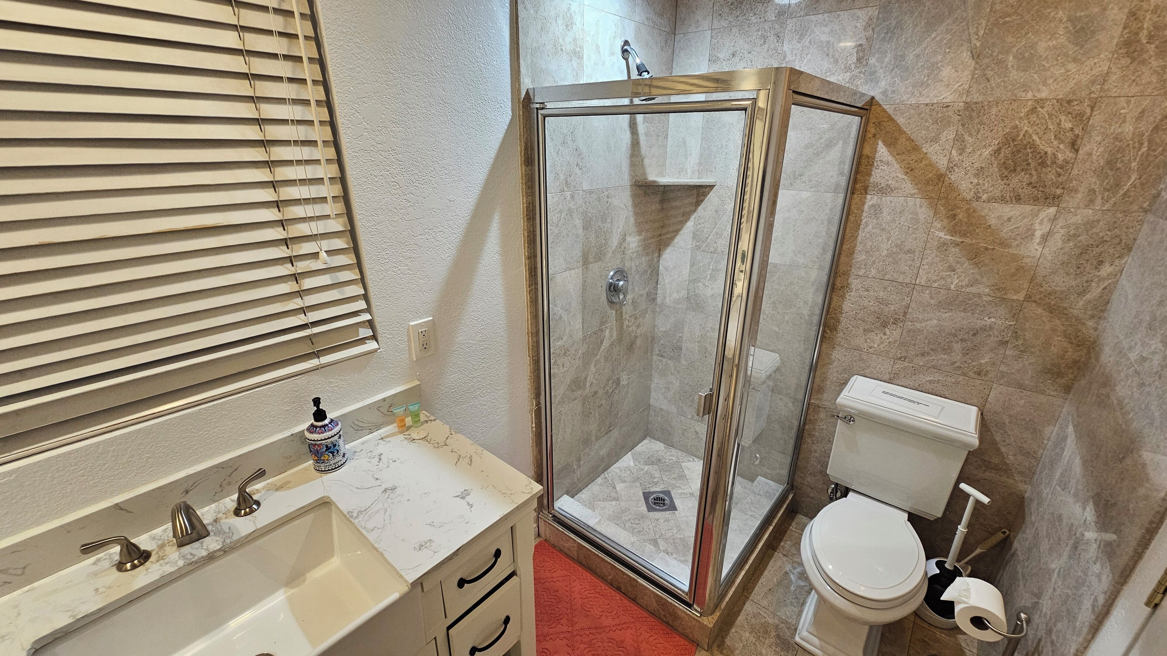 A bathroom with a glass shower enclosure, a toilet, and a sink with a marble countertop.