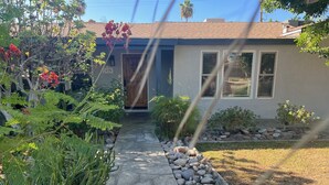 A residential house with a stone pathway leading to the front door, surrounded by various plants and cacti. - Palm Springs Oasis! Private, spacious, pool, spa, sauna shower! (Palm Springs)