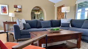 A living room with a sectional sofa, a wooden coffee table with a woven basket, and a red armchair. - Palm Springs Oasis! Private, spacious, pool, spa, sauna shower! (Palm Springs)
