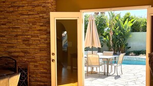 A room with a stone wall, a sliding glass door leading to an outdoor patio with a pool, chairs, and an umbrella. - Palm Springs Oasis! Private, spacious, pool, spa, sauna shower! (Palm Springs)
