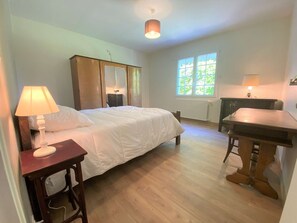A bedroom with a bed, bedside table, lamp, wardrobe, and a window with natural light.