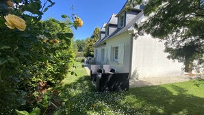 Una casa con jardín, un patio con mobiliario exterior y un cielo azul despejado.