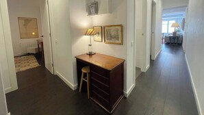 Un couloir avec un bureau, un tabouret, des tableaux encadrés et un radiateur.