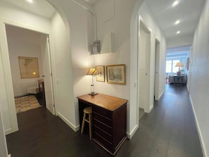 Un couloir avec un bureau, un tabouret, des tableaux encadrés et un radiateur.