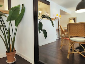 A room with a potted plant, a wicker chair, a dining table, and a lamp.