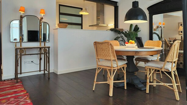 Un coin repas avec une table ronde, des chaises en osier, un saladier de fruits et un ordinateur portable.