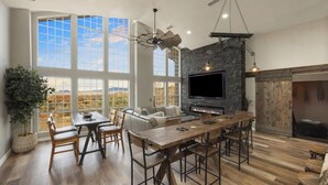 A spacious living area with a large TV, fireplace, and dining table. - Lynx Lake Luxe Vacation Rental Wrapped in Modern Elegance | 6-BR House , Prescott | Sleeps 22 • Hot Tub • Game Rm • EV Charger • Horse Stalls (Prescott)