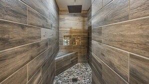 A narrow shower area with wooden walls and a pebble-patterned floor. - Lynx Lake Luxe Vacation Rental Wrapped in Modern Elegance | 6-BR House , Prescott | Sleeps 22 • Hot Tub • Game Rm • EV Charger • Horse Stalls (Prescott)