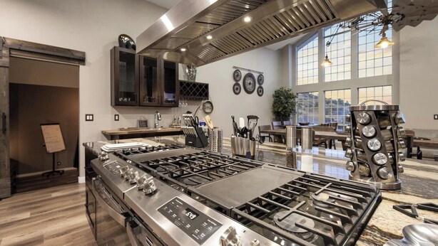 A modern kitchen with a large gas stove, stainless steel appliances, and a view of the city through large windows. - Lynx Lake Luxe Vacation Rental Wrapped in Modern Elegance | 6-BR House , Prescott | Sleeps 22 • Hot Tub • Game Rm • EV Charger • Horse Stalls (Prescott)