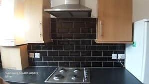 Una cocina con salpicadero de azulejos negros, una campana extractora de acero inoxidable y un refrigerador blanco.