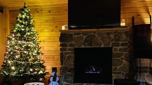 Ein gemütliches Wohnzimmer mit Kamin aus Stein, einem Weihnachtsbaum und einem runden Tisch mit Kerzen und Gläsern.